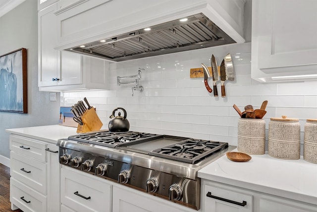 kitchen featuring stainless steel gas stovetop, wall chimney range hood, white cabinets, and tasteful backsplash