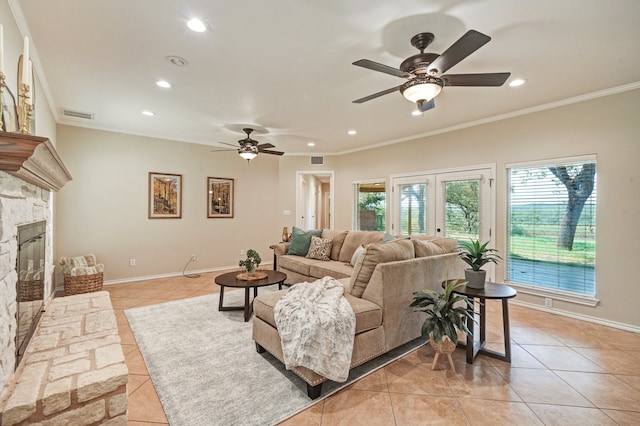 living room with a stone fireplace, crown molding, light tile patterned floors, and ceiling fan