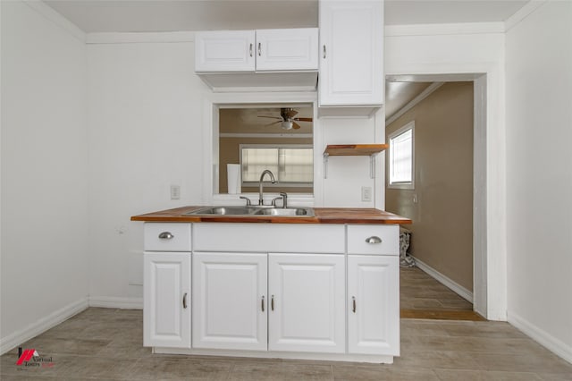 kitchen featuring ceiling fan, white cabinets, ornamental molding, sink, and butcher block counters