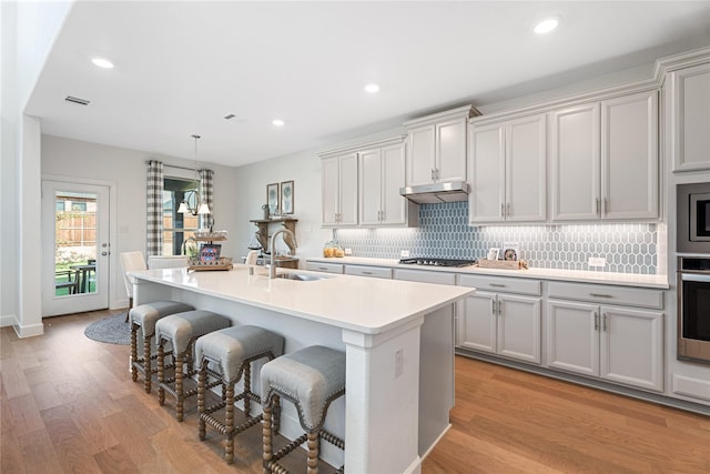 kitchen with stainless steel appliances, sink, light wood-type flooring, a breakfast bar, and a center island with sink