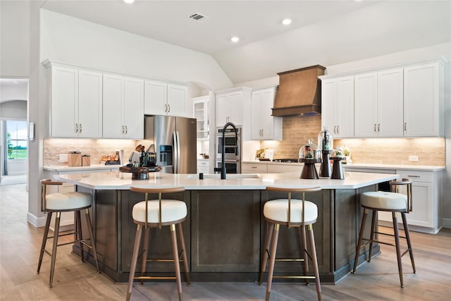 kitchen featuring premium range hood, white cabinetry, an island with sink, a kitchen breakfast bar, and stainless steel appliances