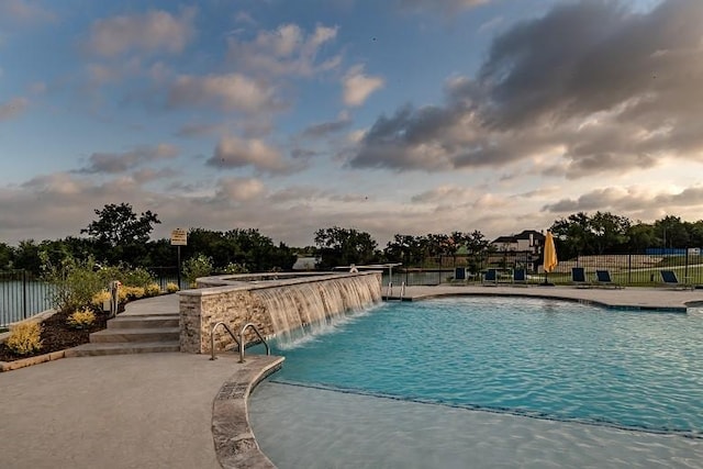 pool at dusk with pool water feature and a patio