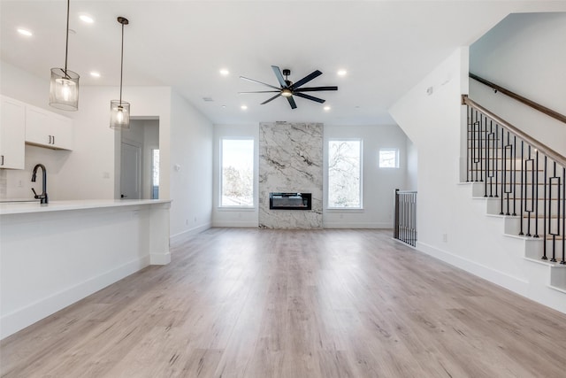 unfurnished living room with ceiling fan, light wood-type flooring, a premium fireplace, and sink