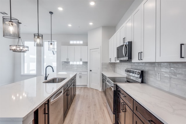 kitchen with dark brown cabinetry, stainless steel appliances, sink, a center island with sink, and white cabinets