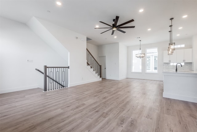 unfurnished living room featuring ceiling fan with notable chandelier, light wood-type flooring, and sink