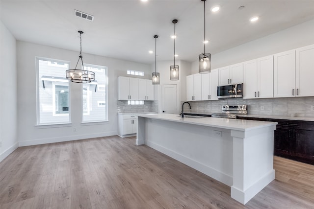 kitchen with a center island with sink, white cabinets, light hardwood / wood-style flooring, decorative light fixtures, and stainless steel appliances