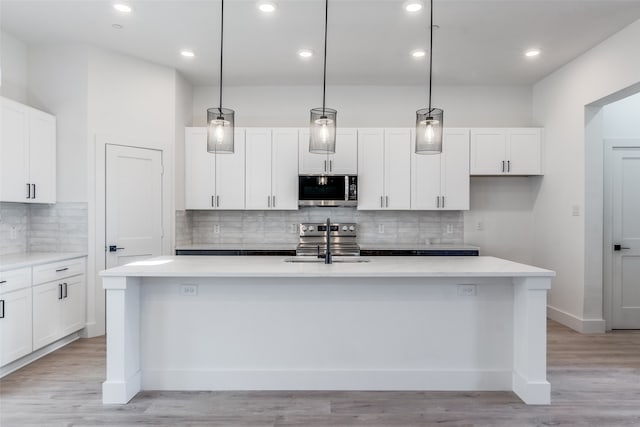 kitchen with stainless steel appliances, hanging light fixtures, and a center island with sink