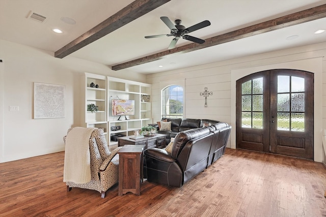 living room featuring beamed ceiling, wood-type flooring, ceiling fan, french doors, and wooden walls