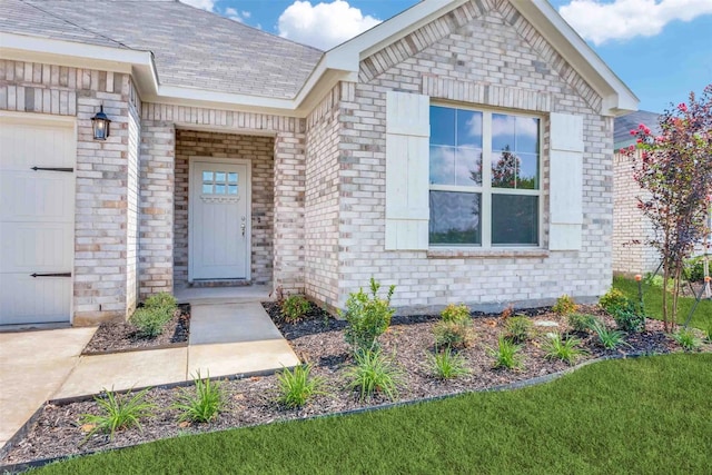 view of exterior entry featuring an attached garage and brick siding