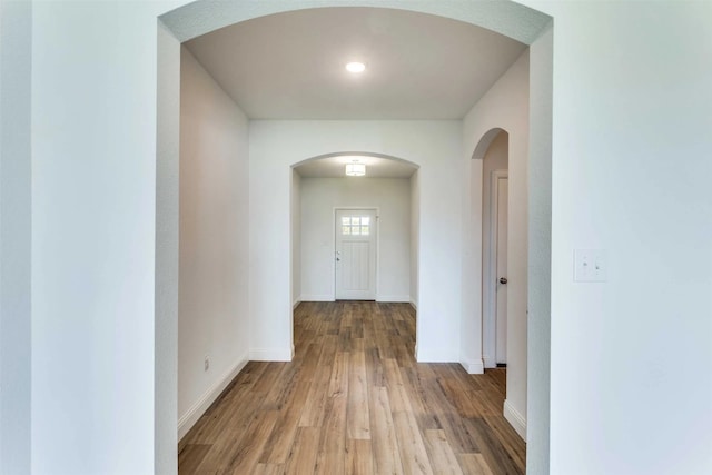 hall with arched walkways, wood finished floors, and baseboards