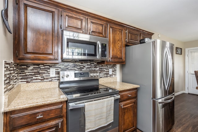 kitchen with appliances with stainless steel finishes, backsplash, light stone countertops, dark brown cabinetry, and dark hardwood / wood-style floors