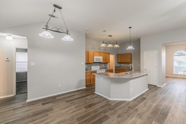 kitchen with a center island with sink, hanging light fixtures, brown cabinetry, a sink, and white appliances