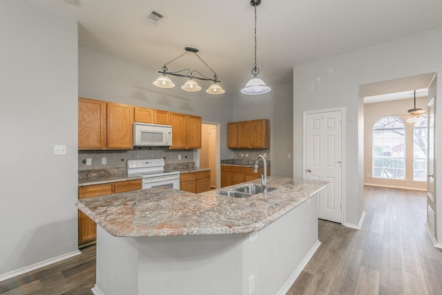 kitchen with white appliances, a center island with sink, visible vents, decorative light fixtures, and a sink