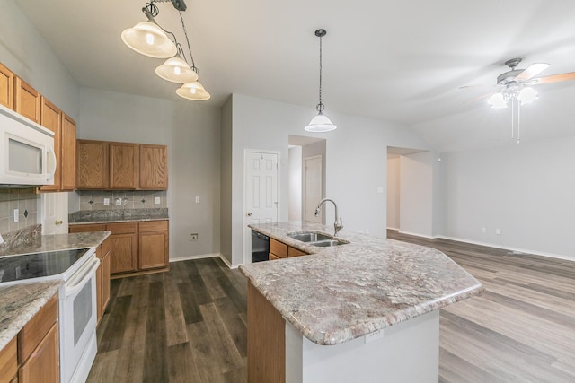 kitchen featuring white appliances, a center island with sink, decorative backsplash, pendant lighting, and a sink