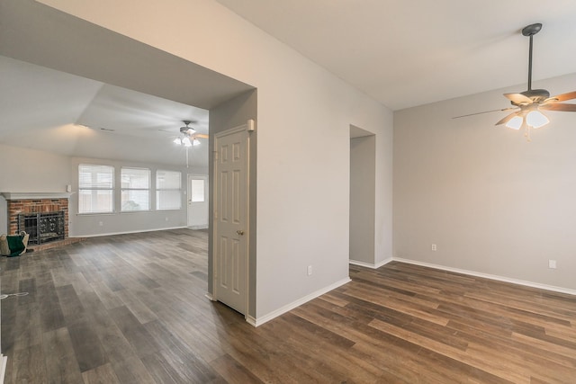 unfurnished living room with dark wood-type flooring, a fireplace, a ceiling fan, and baseboards