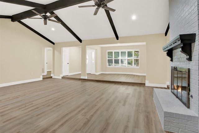 unfurnished living room featuring light wood-type flooring, beam ceiling, high vaulted ceiling, a brick fireplace, and ceiling fan