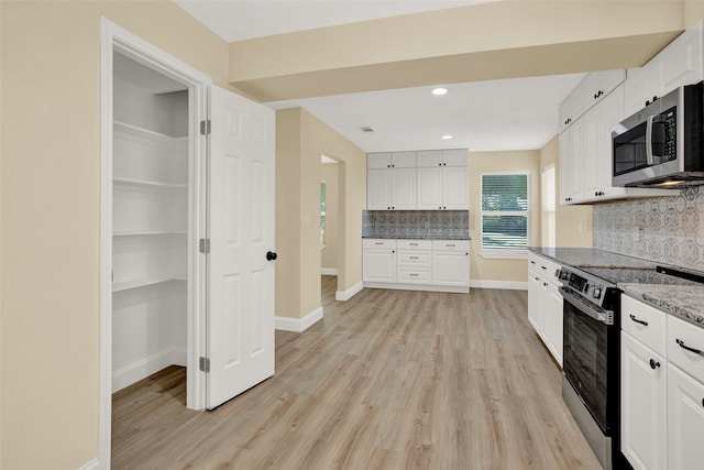 kitchen with decorative backsplash, stainless steel appliances, white cabinets, and light hardwood / wood-style floors