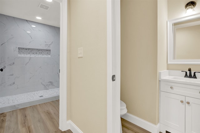 bathroom featuring wood-type flooring, toilet, vanity, and tiled shower