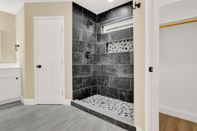 bathroom with a tile shower, vanity, and wood-type flooring