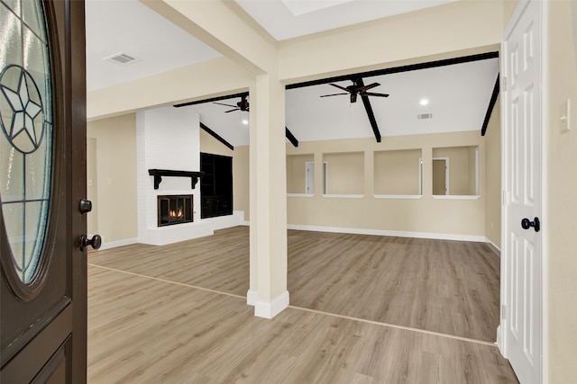 foyer entrance with a brick fireplace, vaulted ceiling with beams, and light hardwood / wood-style floors