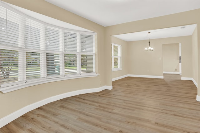 spare room with a notable chandelier and light hardwood / wood-style floors