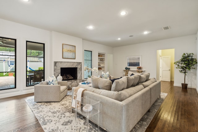 living room featuring built in shelves, a high end fireplace, and dark hardwood / wood-style floors