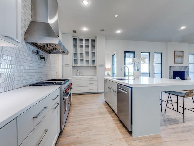 kitchen with a kitchen breakfast bar, light countertops, stainless steel appliances, wall chimney range hood, and a sink