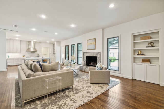 living room with a high end fireplace, dark wood-type flooring, and built in features