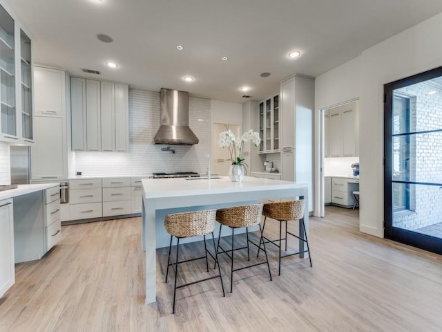 kitchen featuring light wood-style floors, wall chimney exhaust hood, tasteful backsplash, and light countertops