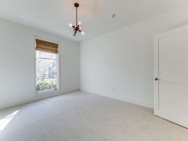 spare room featuring baseboards, a chandelier, and light colored carpet