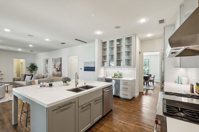 kitchen featuring dark wood-type flooring, sink, wall chimney exhaust hood, backsplash, and a center island with sink