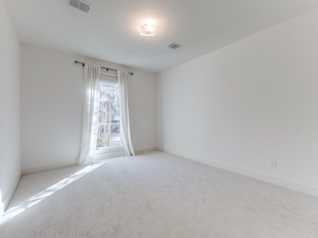 empty room featuring light colored carpet, visible vents, and baseboards