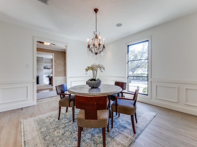 dining space featuring a large fireplace, light wood finished floors, a wainscoted wall, and a chandelier