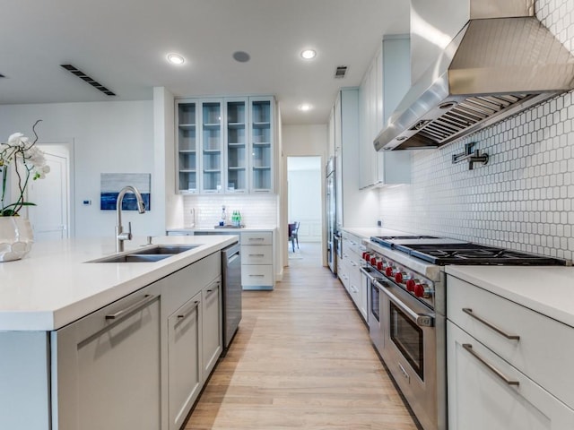 kitchen featuring visible vents, appliances with stainless steel finishes, light wood-style floors, a sink, and wall chimney range hood