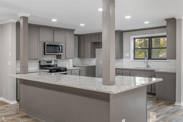 kitchen with appliances with stainless steel finishes, gray cabinets, hardwood / wood-style flooring, and sink