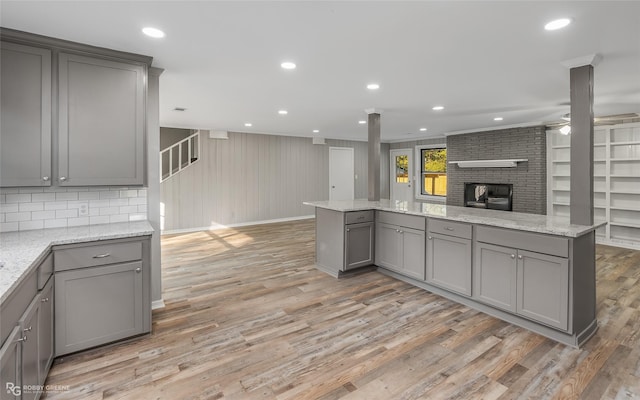 kitchen featuring gray cabinetry, light hardwood / wood-style flooring, ceiling fan, a fireplace, and light stone counters