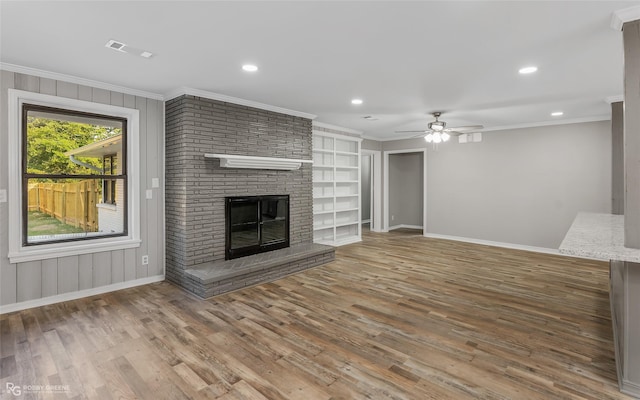 unfurnished living room featuring ceiling fan, built in features, hardwood / wood-style floors, a fireplace, and ornamental molding