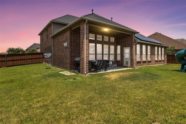 back house at dusk featuring a patio and a yard