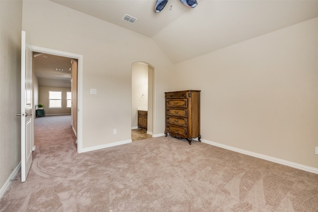 unfurnished bedroom featuring light colored carpet, lofted ceiling, and connected bathroom