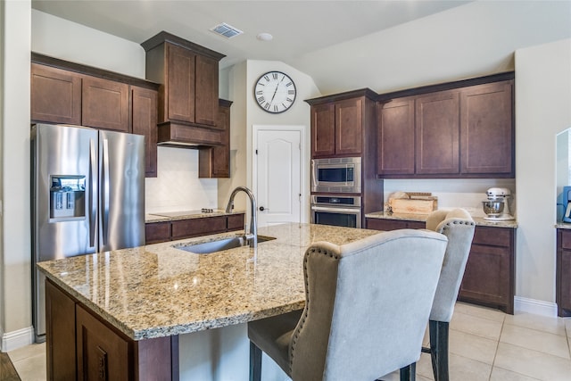 kitchen with light stone counters, a kitchen island with sink, sink, lofted ceiling, and appliances with stainless steel finishes