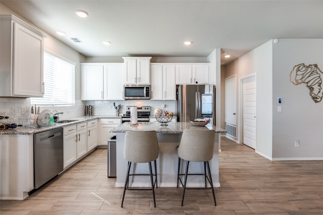 kitchen with appliances with stainless steel finishes, white cabinetry, a center island, and light stone counters