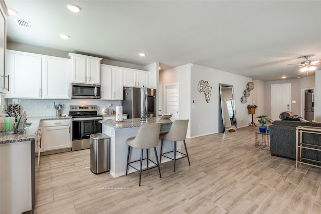 kitchen with ceiling fan, stainless steel appliances, white cabinetry, and a kitchen island