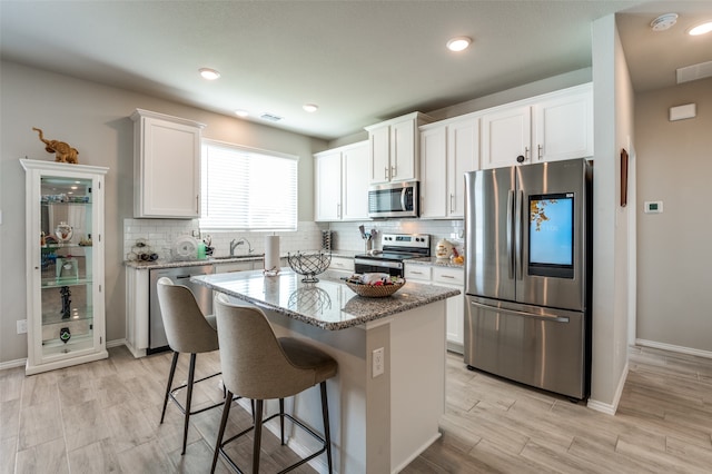 kitchen featuring light stone counters, white cabinets, sink, a kitchen island, and stainless steel appliances