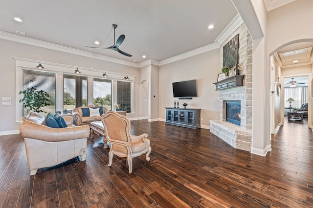 living room with ceiling fan, a stone fireplace, dark hardwood / wood-style floors, and ornamental molding