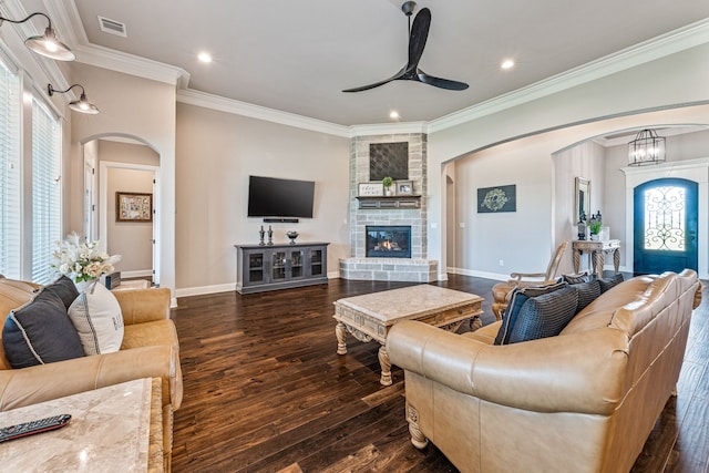 living room featuring ceiling fan with notable chandelier, a stone fireplace, crown molding, and dark hardwood / wood-style floors