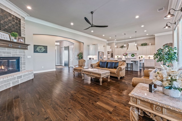 living room with a stone fireplace, ornamental molding, dark hardwood / wood-style flooring, and ceiling fan