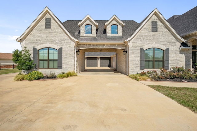 french country home with a shingled roof, driveway, a garage, and stone siding