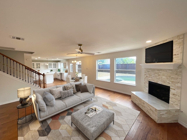 living room with ceiling fan with notable chandelier, wood-type flooring, and a fireplace