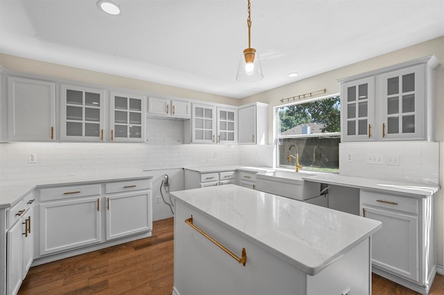 kitchen with light stone counters, a center island, dark wood-type flooring, pendant lighting, and sink