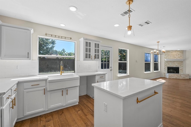 kitchen with white cabinets, dark wood-type flooring, a fireplace, decorative light fixtures, and a center island